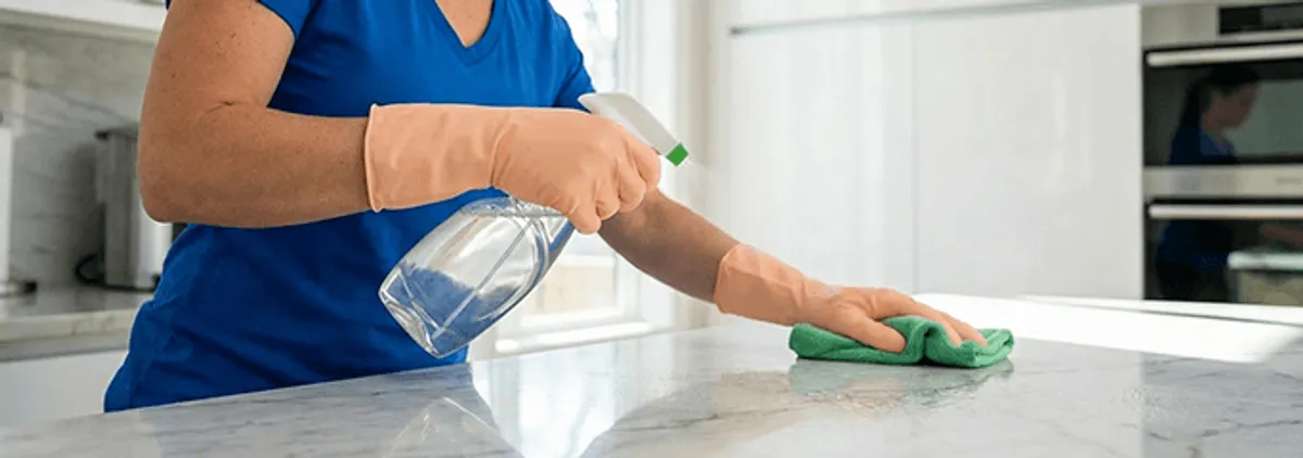 Maid service worker spraying and wiping a kitchen countertop with a microfiber cloth for sanitizing, Staten Island, NY.